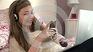 Teenage Girl Lying On Bed Using Laptop Whilst Texting