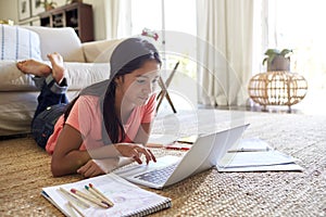 Teenage girl lying on the floor in the living room doing her homework using a laptop computer, low angle, close up