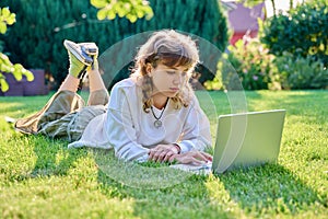 Teenage girl lying on the grass using a laptop