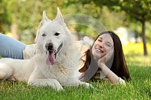 Teenage girl lying with white Swiss Shepherd dog on green grass in park