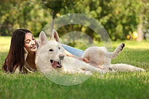 Teenage girl lying with white Swiss Shepherd dog on green grass in park