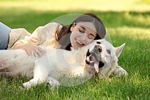 Teenage girl lying with white Swiss Shepherd dog on green grass in park