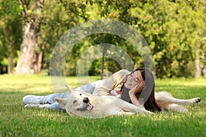 Teenage girl lying with white Swiss Shepherd dog on green grass in park