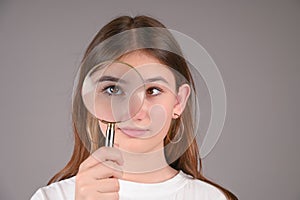 Teenage girl with magnifying glass on gray background. Female eyes with strabismus
