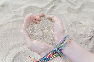 Teenage girl making a heart with her hands and sand