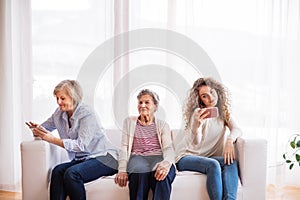A teenage girl, mother and grandmother with smartphone at home.