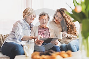 A teenage girl, mother and grandmother with tablet at home.