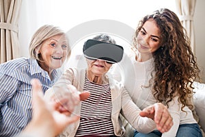 A teenage girl, mother and grandmother with VR goggles at home.