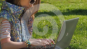 A teenage girl on nature with a laptop. The girl in the park is working on a laptop. Hands in bracelets