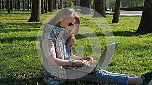 A teenage girl on nature with a laptop. The girl in the park is working on a laptop. Hands in bracelets.