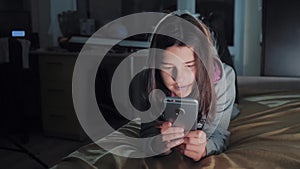 Teenage girl online shopping looks on her smartphone in bed during the night. lifestyle little teen hood girl writes a