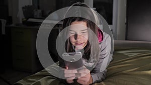 Teenage girl online shopping looks on her smartphone in bed during the night. little teen hood girl writes lifestyle a