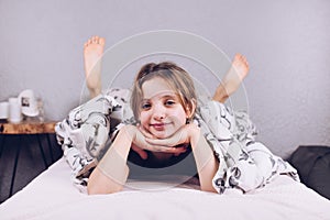 A teenage girl in pajamas lies on the bed with her head in her hands. Smiling. The child is covered with a blanket.