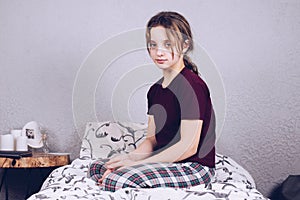 A teenage girl in pajamas is sitting on the bed and smiling.