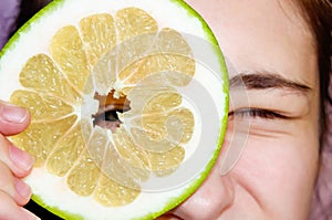 A teenage girl peeks through the hole in the middle of a sliced Citrus Sweetie, holding it up to her eye