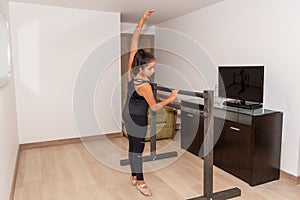 A teenage girl performs a ballet move with an internet class in her living room