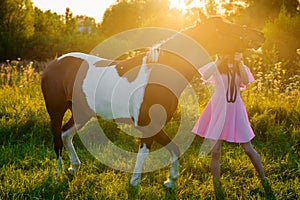 Teenage girl in pink dress walking with a horse at sunset