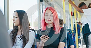 A teenage girl with pink hair sits in a chair on a public transit bus