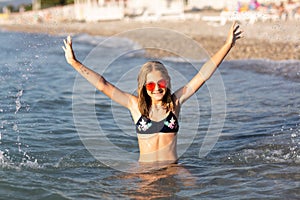 Teenage girl in pink sunglasses having fun on the beach in the sea, playing with splashes. Fun on summer hloiday concept