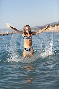 Teenage girl in pink sunglasses having fun on the beach in the sea, playing with splashes. Fun on summer hloiday concept