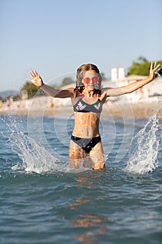 Teenage girl in pink sunglasses having fun on the beach in the sea, playing with splashes. Fun on summer hloiday concept