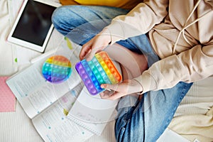 Teenage girl playing with rainbow pop-it fidget toy while studying at home. Teen kid with trendy stress and anxiety relief