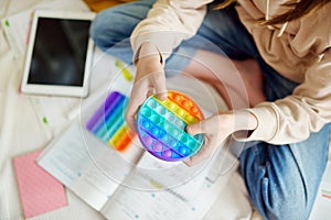 Teenage girl playing with rainbow pop-it fidget toy while studying at home. Teen kid with trendy stress and anxiety relief photo