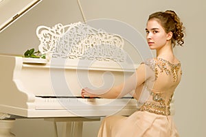 A teenage girl is playing on a white grand piano.