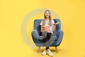 Teenage girl with popcorn sitting in armchair during cinema show