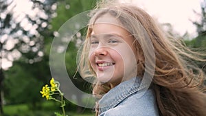 Teenage girl portrait on the background of green trees. Charming young girl enjoying beautiful day with yellow flower in hand