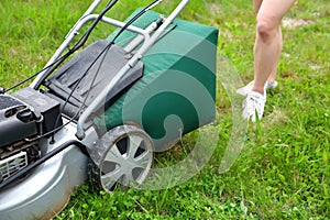 Teenage girl pruning green high grass with the help of an petrol lawn mower.