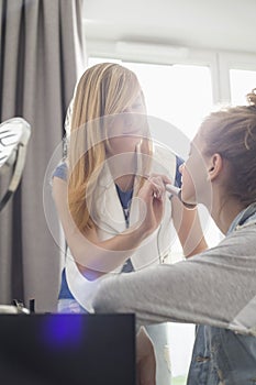 Teenage girl putting makeup on sister at home