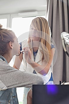 Teenage girl putting makeup on sister at home