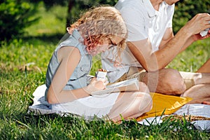 Teenage girl reading book on grass during family picnic in the gardens