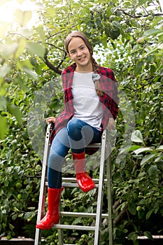Teenage girl in red gumboots posing on ladder at apple garden