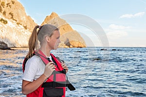 Teenage girl in red life jacket stands on ocean and looks at sea. Means of rescuing people on water, buoyancy and safety