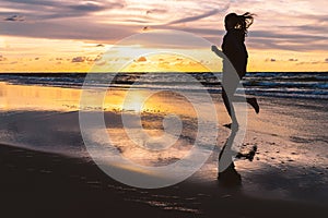 Teenage girl running barefoot on a sandy beach at sunset - a silhouetted photo of a young woman against the sky