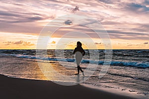 Teenage girl running barefoot on a sandy beach at sunset - a silhouetted photo of a young woman against the sky