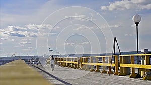 Teenage girl runs on sea pier to sea gulls