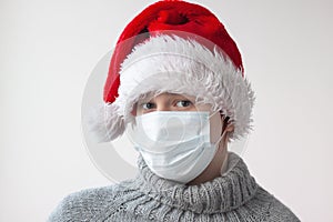 A teenage girl in a Santa hat and a gray sweater wearing a medical mask. Safe Christmas and New year concept