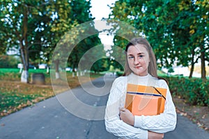 Teenage girl schoolgirl, teenager white sweater summer city, warm sweater, hands notebooks books and folders, smiling