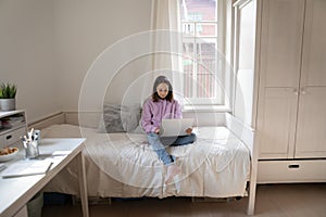 Teenage girl sit on bed using laptop browsing web
