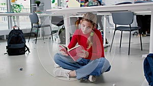 Teenage girl sit on floor in classroom and read book