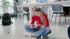 Teenage girl sit on floor in classroom and read book or diary preparing for exam during break at school