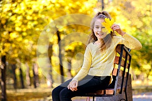 A teenage girl sits on a bench in an autumn park, wearing a yellow sweater, golden autumn, cheerful blonde girl