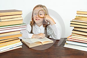 A teenage girl sits among the books and looks through a magnifying glass