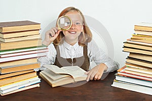 A teenage girl sits among the books and looks through a magnifying glass