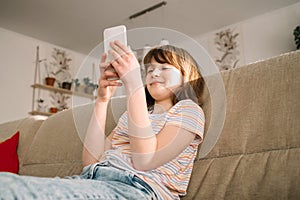 A teenage girl sits on the couch at home and uses a mobile phone, chatting and calling friends. Teenagers and technology