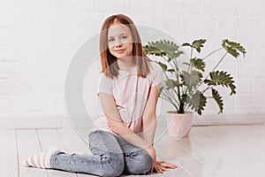 Teenage girl sits on the floor in a white room and looks into the camera