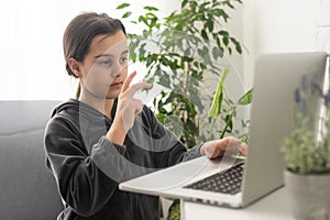 A teenage girl sits in front of her laptop learning sign language, a language for the deaf online